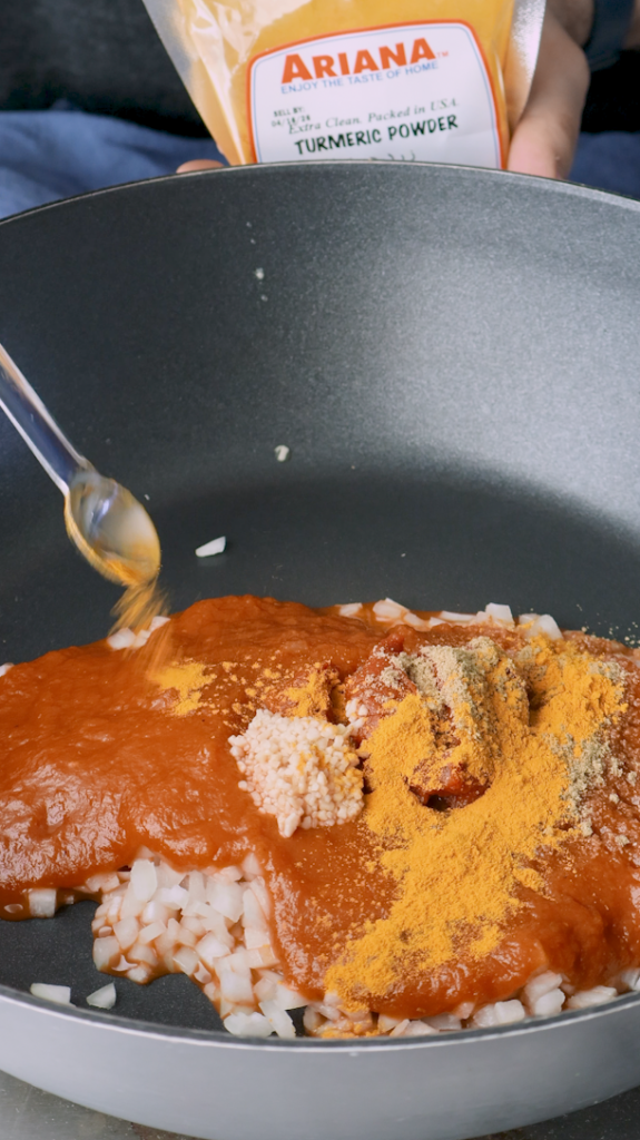 Next add diced onion, tomato sauce, tomato paste, minced garlic, turmeric, and coriander to a large pan. 